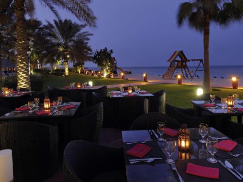a restaurant with tables and chairs with a view of the ocean at Mövenpick Hotel & Resort Al Bida'a in Kuwait