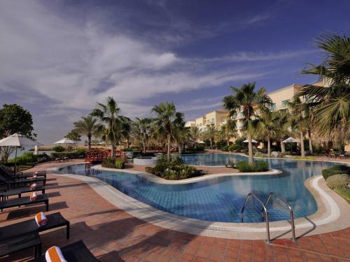 a large swimming pool with palm trees in a resort at Mövenpick Hotel & Resort Al Bida'a in Kuwait
