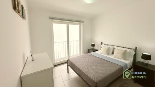 a white bedroom with a bed and a window at Terraço e vista deslumbrante no centro de Angra in Angra do Heroísmo