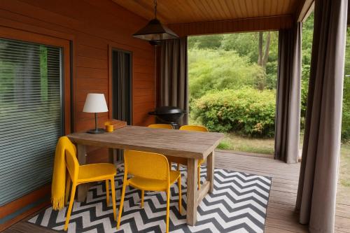 a wooden table and yellow chairs on a porch at Gezellig chalet met 2 slaapkamers aan bosrand in Erm