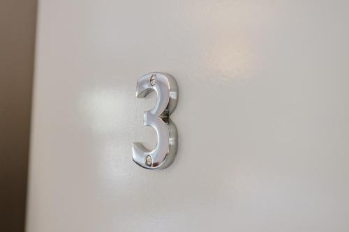 a metal number three on a white door at Grace's Guesthouse 68a in Tring