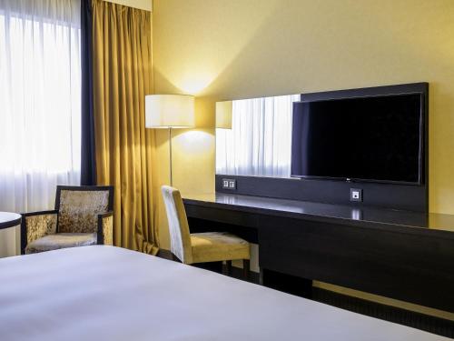 a hotel room with a bed and a desk with a television at Mercure Antwerp City South in Antwerp
