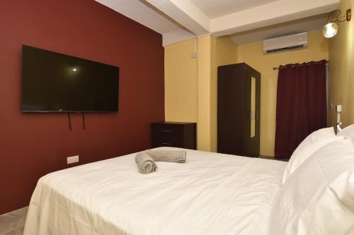 a bedroom with a white bed with a flat screen tv at Good Stay Apartments and Car Rentals in Gros Islet