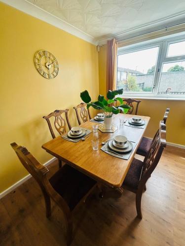 a dining room table with chairs and a clock on the wall at Spacious, 3 double bedroomed, free parking, 9 mins Elland Rd, nr Leeds City Centre in Leeds