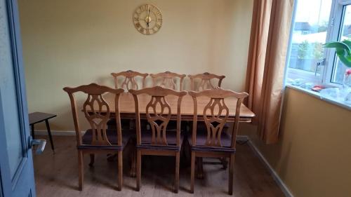 a dining room table with four chairs and a clock on the wall at Spacious, 3 double bedroomed, free parking, 9 mins Elland Rd, nr Leeds City Centre in Leeds