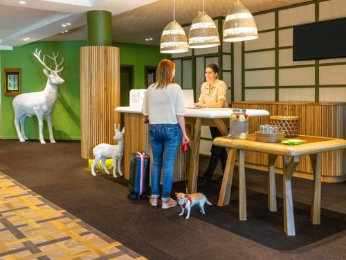 deux femmes debout à un comptoir dans un bureau avec des animaux dans l'établissement Ibis Styles Arlon Porte du Luxembourg, à Arlon