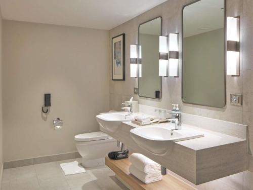 a bathroom with two sinks and a toilet and mirrors at Novotel Suites Manila at Acqua in Manila