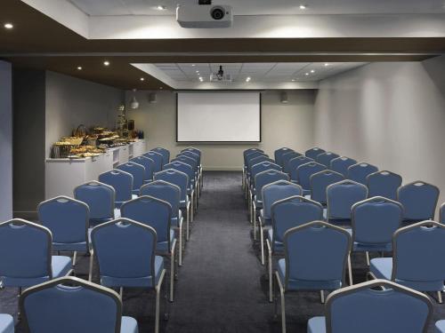 a conference room with blue chairs and a white screen at Adagio Jeddah City Center in Jeddah