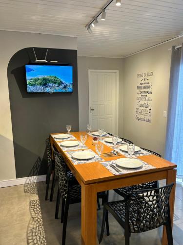 a dining room table with chairs and a television on a wall at Solarium Riviera - Casa2 - NOVA 600m praia Riviera in Matinhos