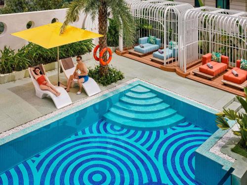 a man and woman sitting under an umbrella next to a swimming pool at Mövenpick Hotel Hanoi Centre in Hanoi