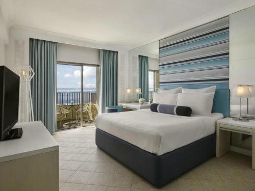 a bedroom with a bed and a television and a balcony at Mövenpick Hotel Mactan Island Cebu in Mactan