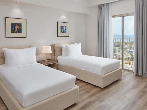 two beds in a hotel room with a balcony at Mövenpick Hotel Mactan Island Cebu in Mactan