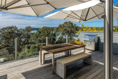 une table et un banc en bois sur une terrasse avec un parasol dans l'établissement The Cottage - Oneroa's Best Viewpoint, à Waiheke Island
