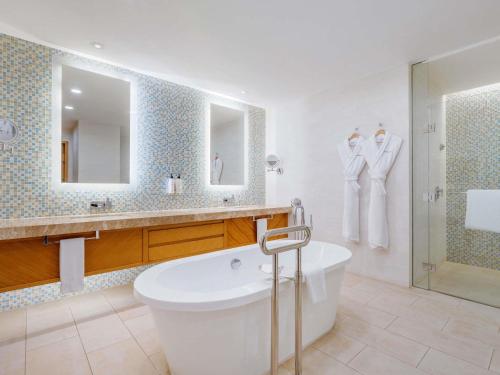 a bathroom with a tub and a shower with two mirrors at Swissôtel Al Ghurair Dubai - Deira & Creek in Dubai