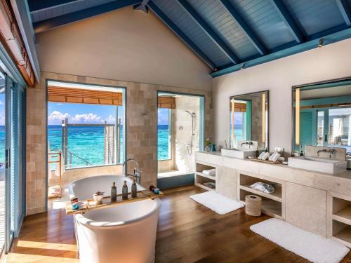 a bathroom with two sinks and a tub with a view of the ocean at Raffles Maldives Meradhoo in Gaafu Alifu Atoll