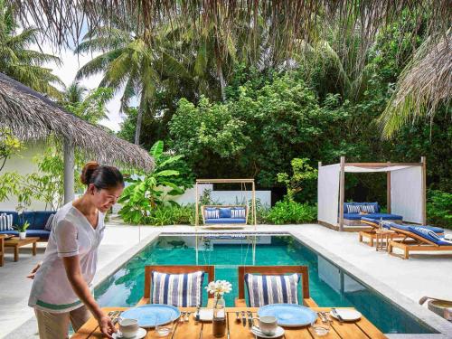 a woman standing in front of a table next to a pool at Raffles Maldives Meradhoo in Gaafu Alifu Atoll