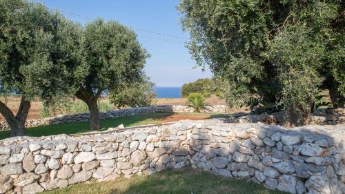 a stone wall with trees and the ocean in the background at Masseria dei Monaci in Otranto