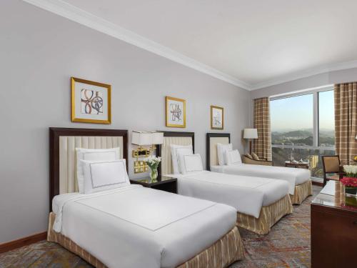 a hotel room with three beds and a window at Swissotel Al Maqam Makkah in Makkah