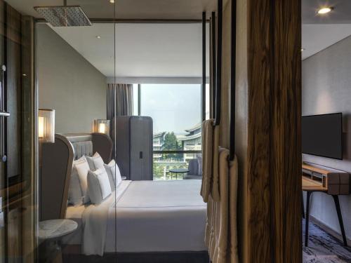 a bedroom with a bed and a desk and a window at Swissôtel Jakarta PIK Avenue in Jakarta