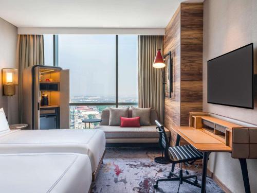 a hotel room with a bed and a desk and a tv at Swissôtel Jakarta PIK Avenue in Jakarta