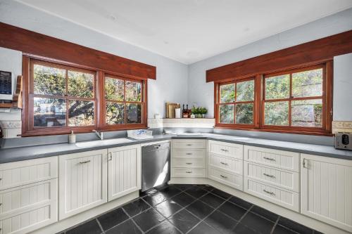 a large kitchen with white cabinets and windows at Cornwall Cottage in Merimbula
