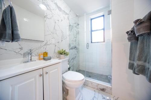 a white bathroom with a toilet and a shower at Modern Apartment By Central Park - 3 BR in New York