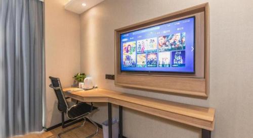 a room with a desk with a television on a wall at GreenTree Inn Express Zhangjiagang Hexing Town Shazhou Professional Institue of Technology in Qiwei