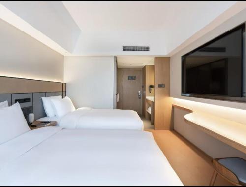 two beds in a hotel room with a flat screen tv at Ji Hotel Guangzhou Zhujiang New Town in Guangzhou