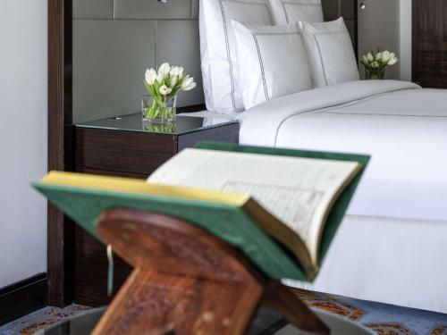 a book on a table next to a bed at Swissotel Makkah in Makkah