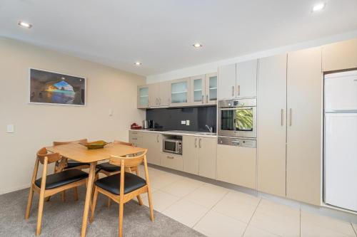 a kitchen with white cabinets and a wooden table and chairs at Esplanade Apartments in Whitianga