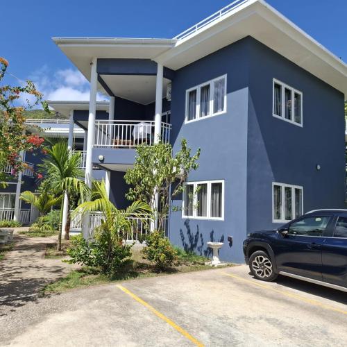 a blue house with a car parked in front of it at Harmony Self-Catering Apartments in Beau Vallon