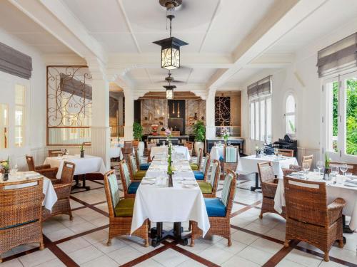 a restaurant with white tables and chairs and windows at Raffles Grand Hotel d'Angkor in Siem Reap