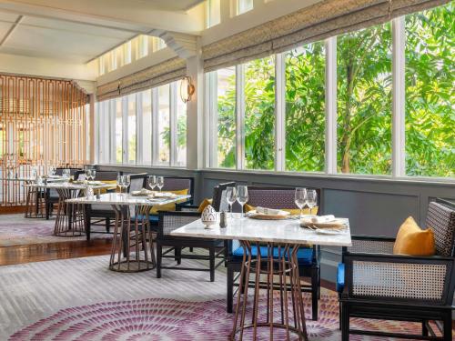 a restaurant with tables and chairs and large windows at Raffles Grand Hotel d'Angkor in Siem Reap