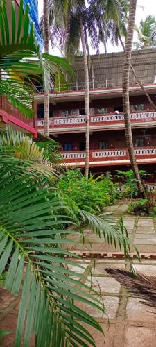 a red building with palm trees in front of it at Samhen guest house in Majorda