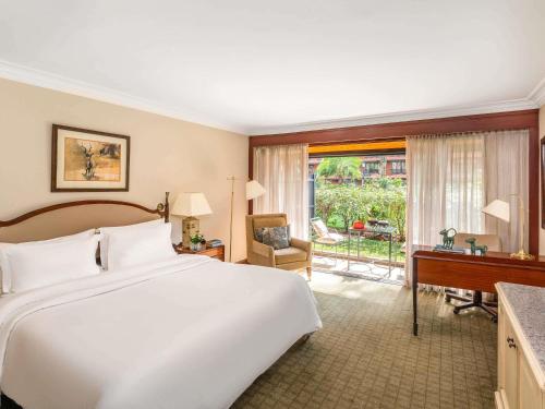 a bedroom with a large white bed and a desk and a window at Fairmont The Norfolk in Nairobi