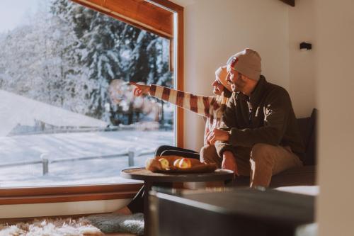 a man and woman sitting in a room looking out a window at Farm Hotel Chalet Grosslehen in Fieberbrunn