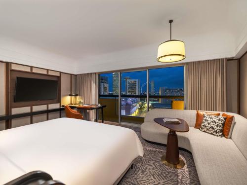 a bedroom with a bed and a couch and a tv at Fairmont Singapore in Singapore