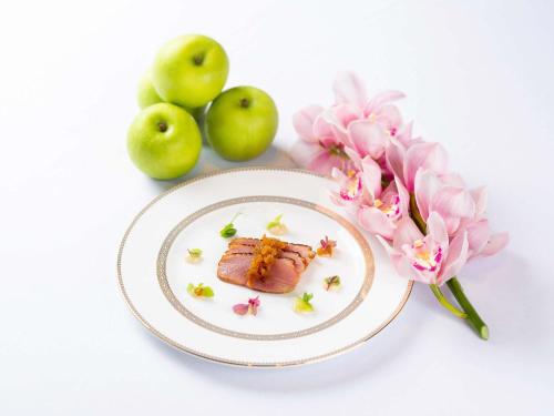 a plate with a piece of meat next to apples and flowers at Raffles Jakarta in Jakarta