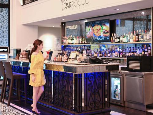 a woman standing at a bar in a restaurant at Mövenpick Myth Hotel Patong Phuket in Patong Beach