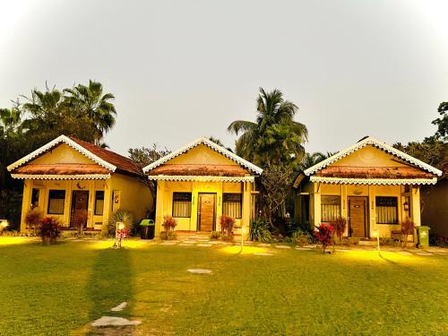 two yellow houses with palm trees in a yard at Breathing Earth - Rooms and Pool in Kolkata
