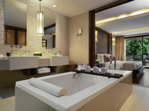 a bathroom with a large tub and a bedroom at Mövenpick Resort Bangtao Beach Phuket in Bang Tao Beach