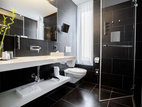 a black bathroom with a toilet and a shower at Mercure Chur City West in Chur
