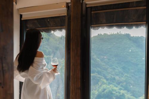 a woman holding a glass of wine looking out a window at Gia Trang Heian Hoa Binh in Hòa Bình