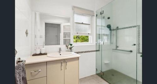 a white bathroom with a sink and a shower at Charming Cottage Walk to City and Eat Street in Braddon