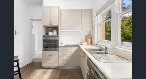 a kitchen with white cabinets and a sink and two windows at Charming Cottage Walk to City and Eat Street in Braddon