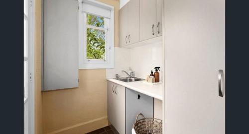 a white kitchen with a sink and a window at Charming Cottage Walk to City and Eat Street in Braddon