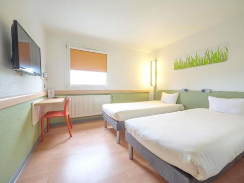 a room with two beds and a desk and a tv at Ibis Budget Sarrebourg Buhl in Sarrebourg
