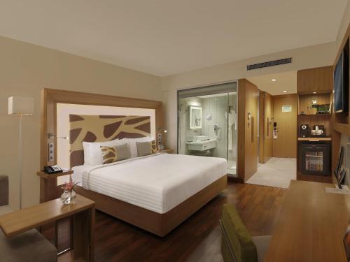 a bedroom with a large bed and a bathroom at Novotel Chennai OMR in Chennai