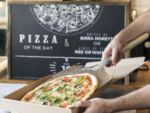 a person cutting a pizza in a box at Novotel London Canary Wharf in London