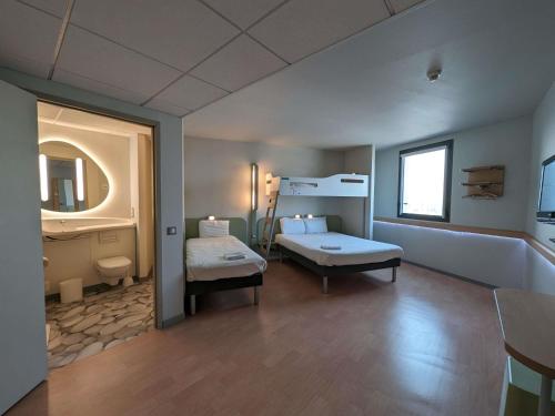 a bedroom with two beds and a sink and a mirror at Ibis Budget Clermont Ferrand - Le Brezet - Aeroport in Clermont-Ferrand